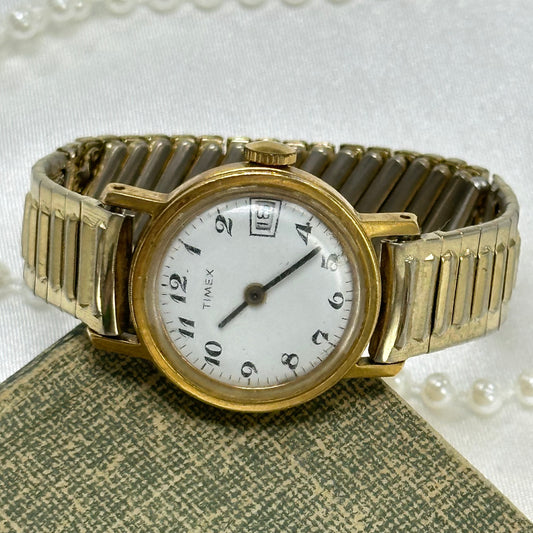 Vintage gold tone round dial manual winding Timex watch with unique stretchable band and date display.