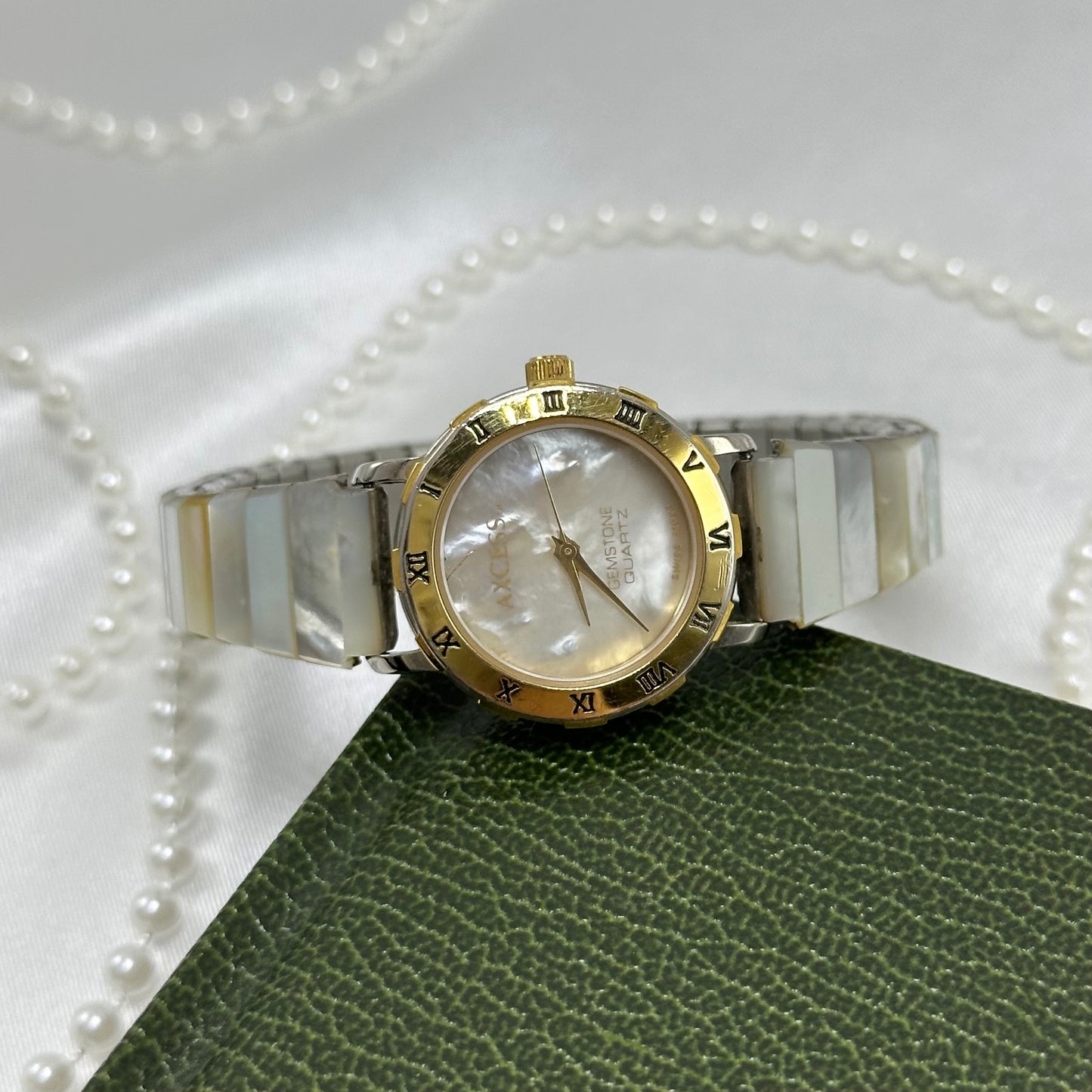 Vintage gold tone watch with round mother of pearl dial and pearl abalone style stretchable band.