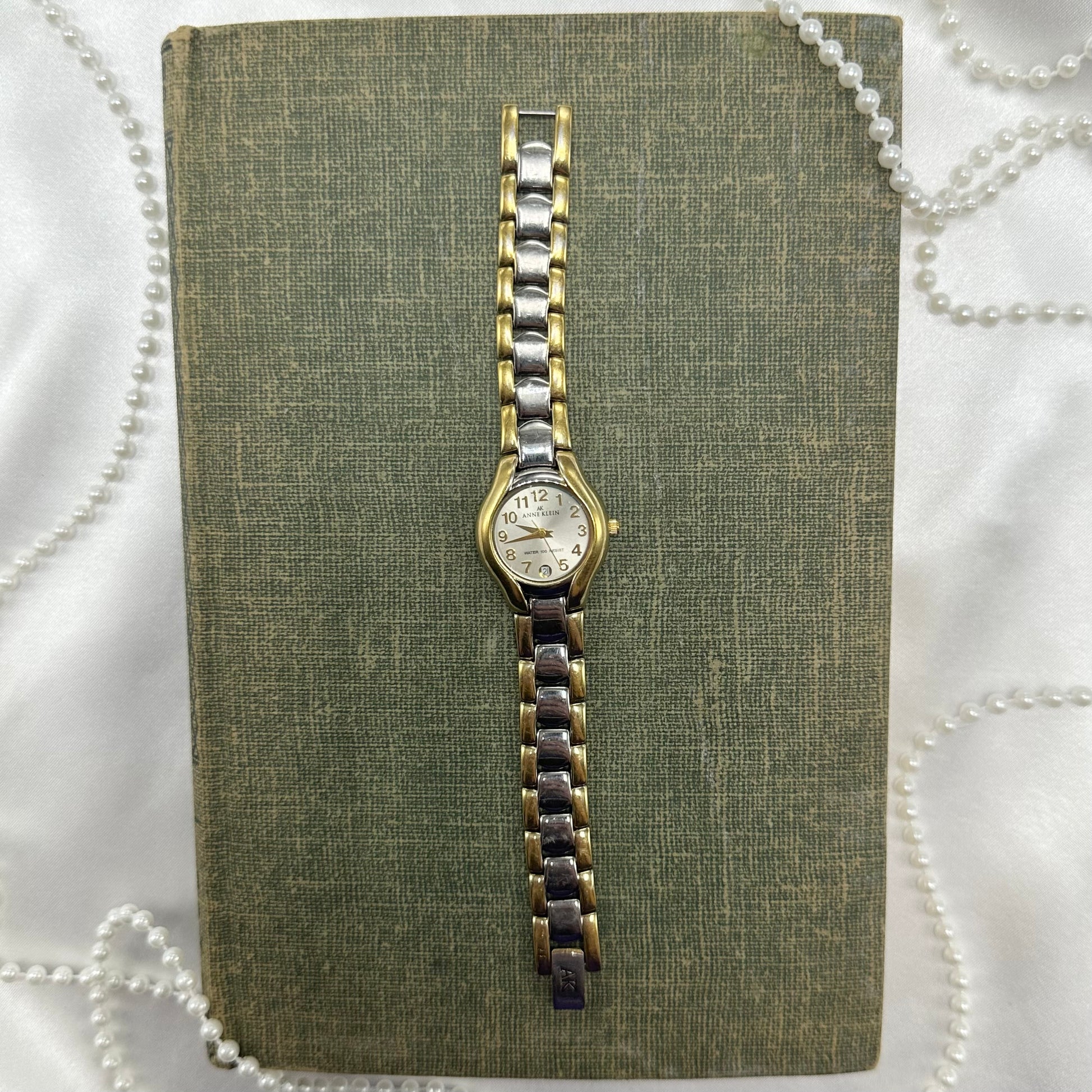 Vintage silver and gold tone Anne Klein watch with date display and clasp band.