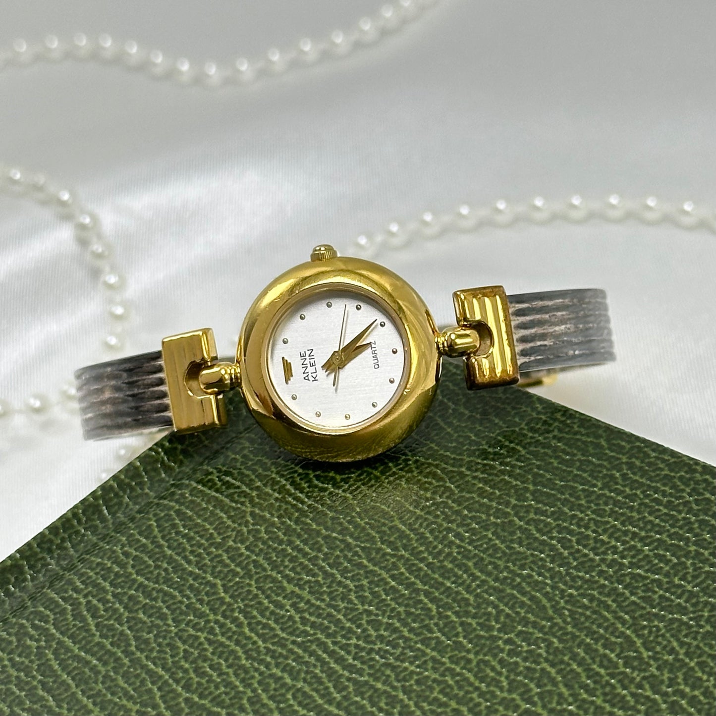 Vintage silver and gold tone Anne Klein watch with hinged bangle band and round dial.