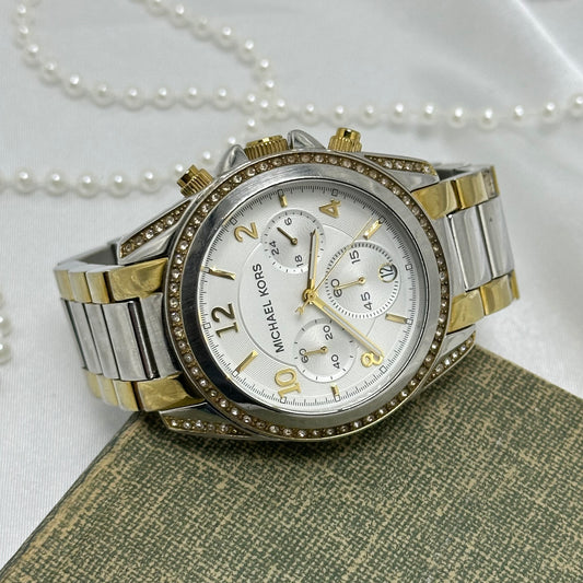 Vintage silver and gold tone Michael Kors MK-5685 tank stainless steel watch with round dial and double locking fold over clasp band. Date display. Buttons on the side start/stop the stopwatch dial at the bottom and reset the stopwatch hand. 10 ATM (100 meter) water resistant.