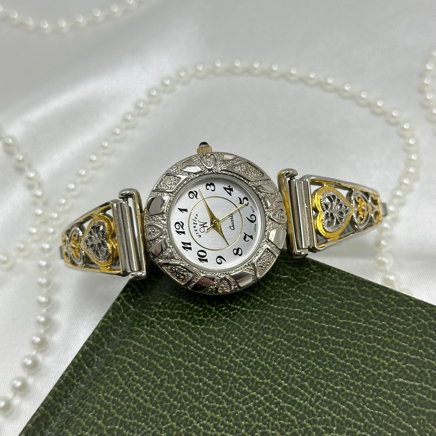 Vintage silver and gold tone Wrangler watch with round dial, two-tone filigree stretchable band, and black jewel crown.