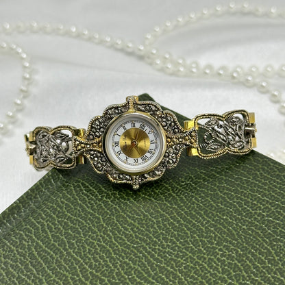 Vintage silver and gold tone art deco style watch with intricate intwined band and roman numeral markers.