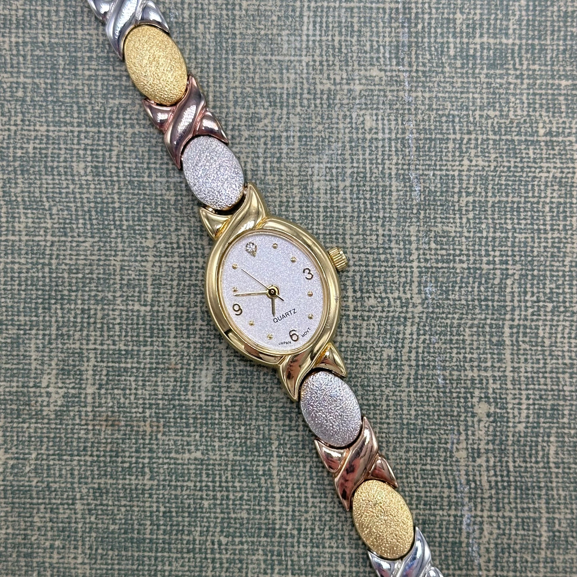 Vintage silver, gold, and bronze tone Avon watch with XO clasp band and oval dial.