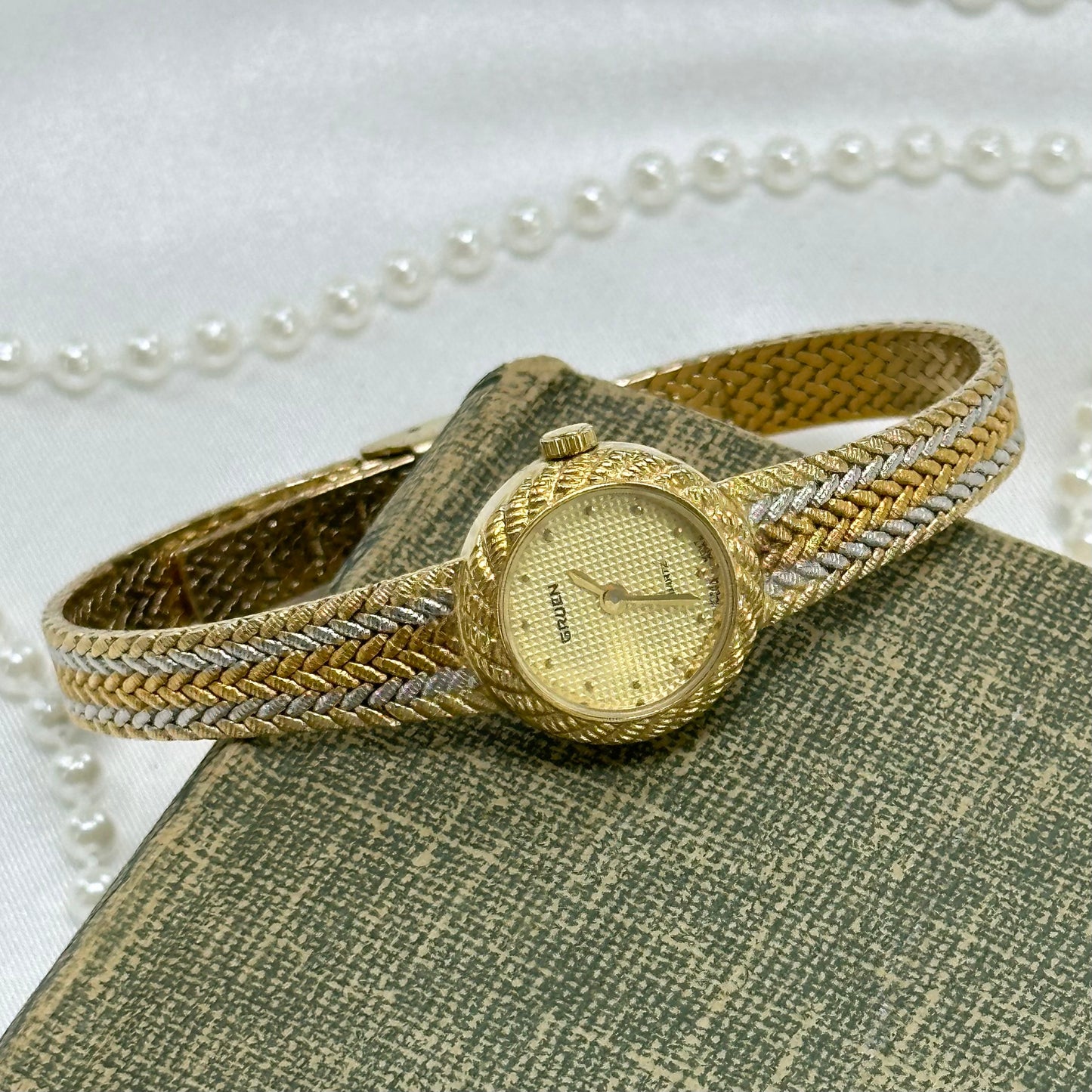 Vintage silver, gold, and bronze tone Gruen watch with tri-tone braided band and dainty round dial.