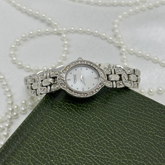 Vintage silver tone Caravelle by Bulova watch with white oval dial, crystal accented bezel and bracelet clasp band.