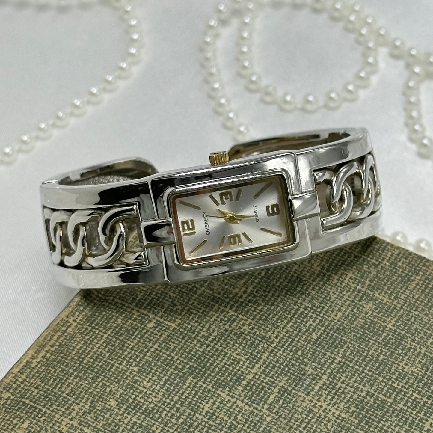 Vintage silver tone Embassy cuff watch with gold markers and crown.