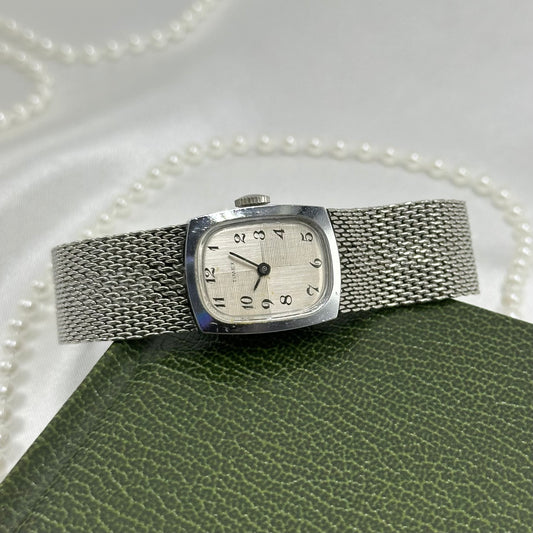 Vintage silver tone mechanical winding Timex watch with mesh band and rectangular dial.