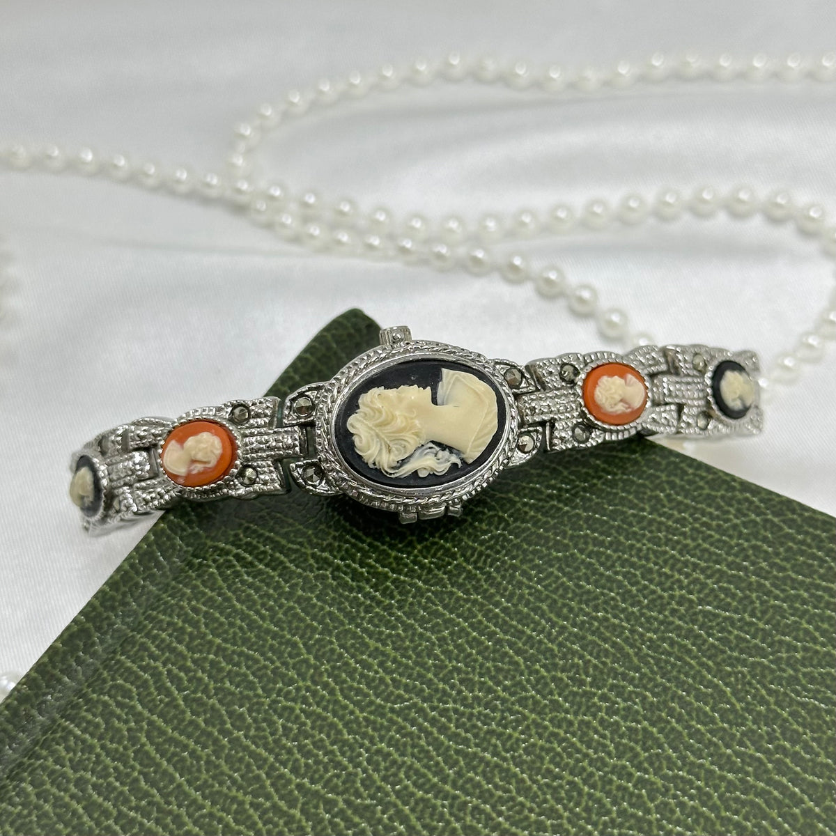 Vintage silver tone peekaboo watch with black and orange cameos and magnetic clasp band.