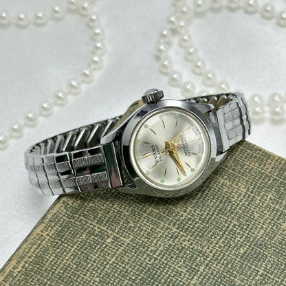 Vintage silver tone round dial Evans De Luxe 27 jewel manual winding Swiss made watch with gold hands and green markers. Band is stretchable. Waterproof and antimagnetic.