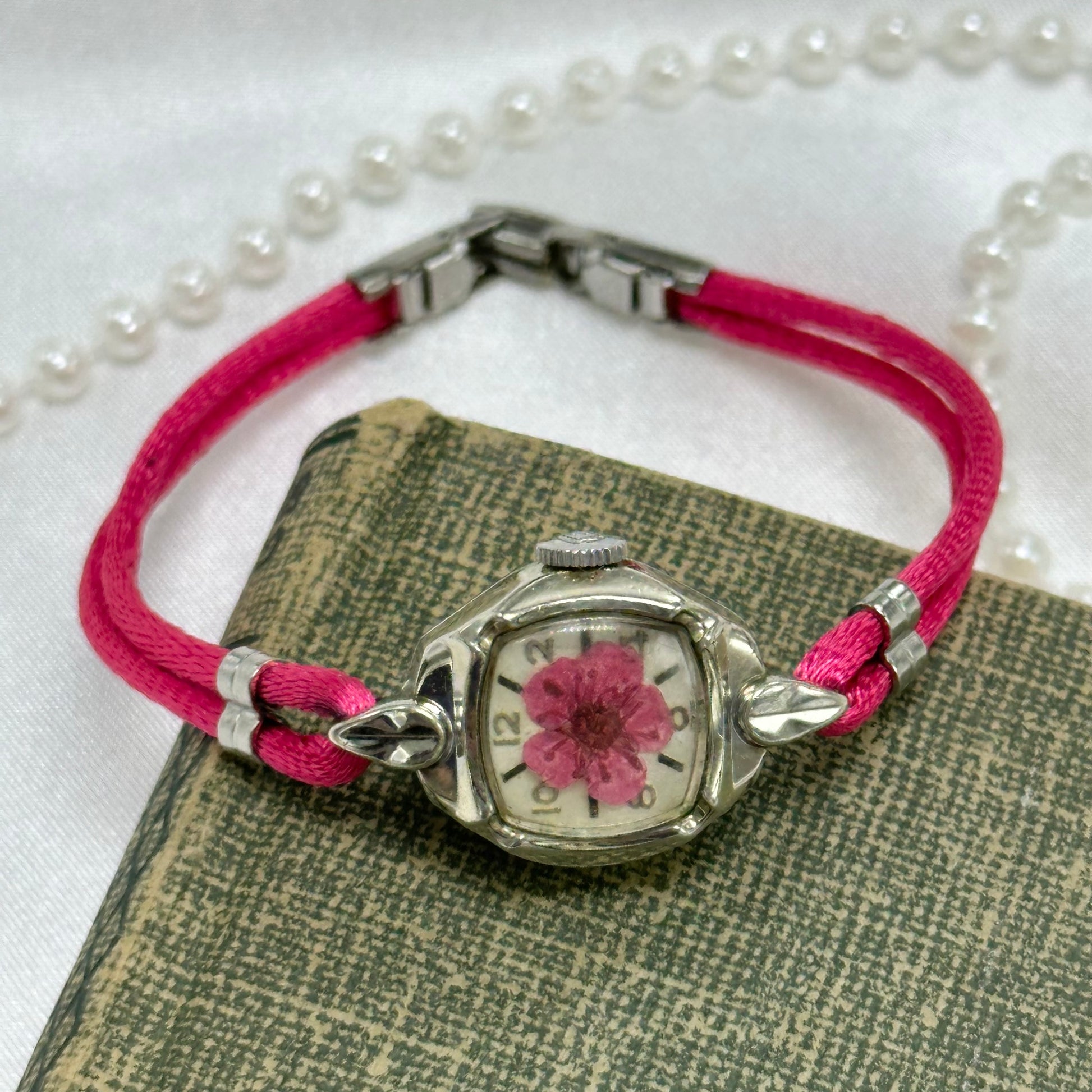 Vintage silver tone wind up watch with round diamanté dial. Pink pressed flower and stain band.