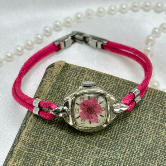 Vintage silver tone wind up watch with round diamanté dial. Pink pressed flower and stain band.